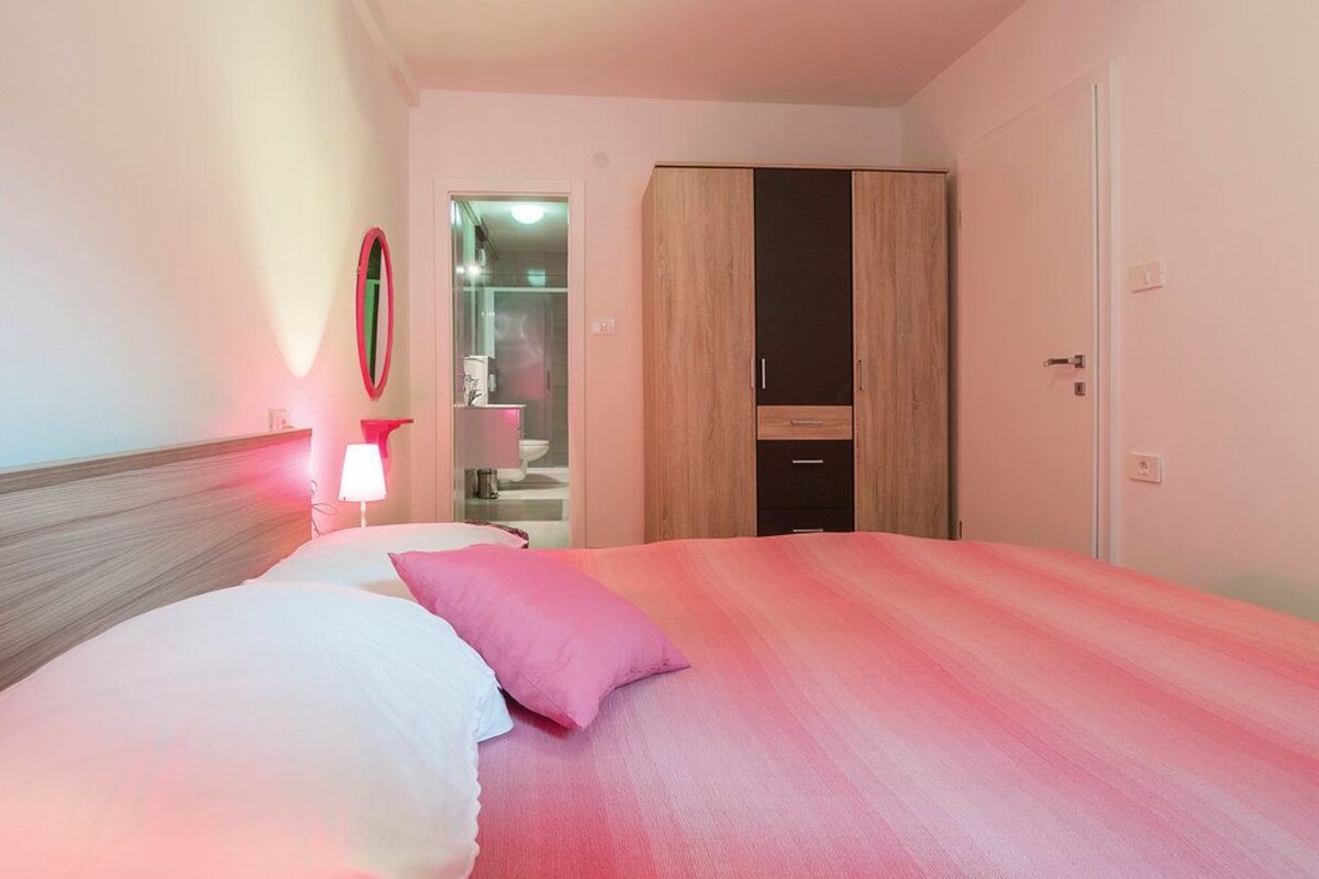 A hotel room with a bed, a bedside lamp, a wardrobe, and a bathroom visible through an open door.