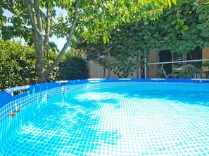 A swimming pool with a blue tiled floor, surrounded by trees and a building in the background. - House 1295 (Marcana)