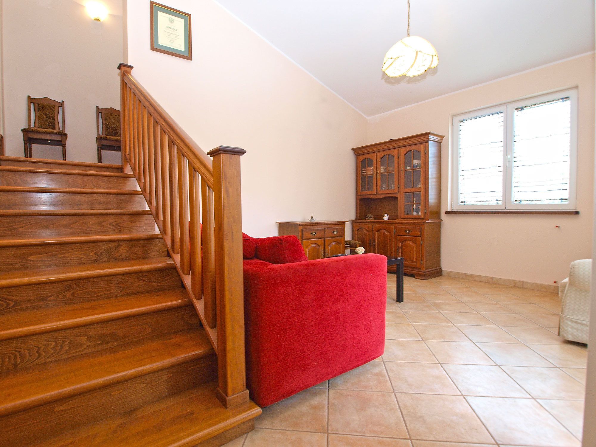 A staircase leading to a landing with a red sofa and a wooden cabinet.