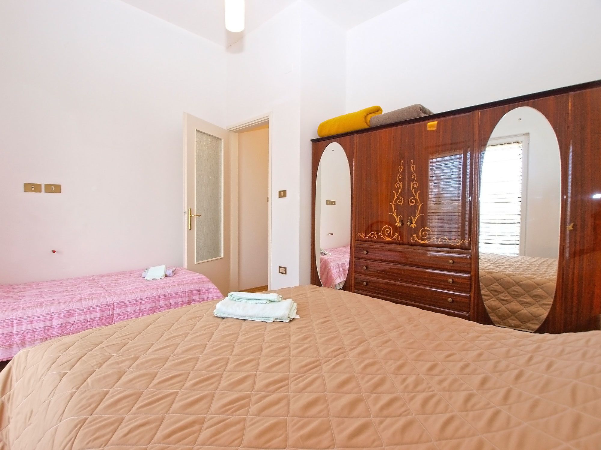 A bedroom with a large bed, a smaller bed, a wardrobe, and a mirror.