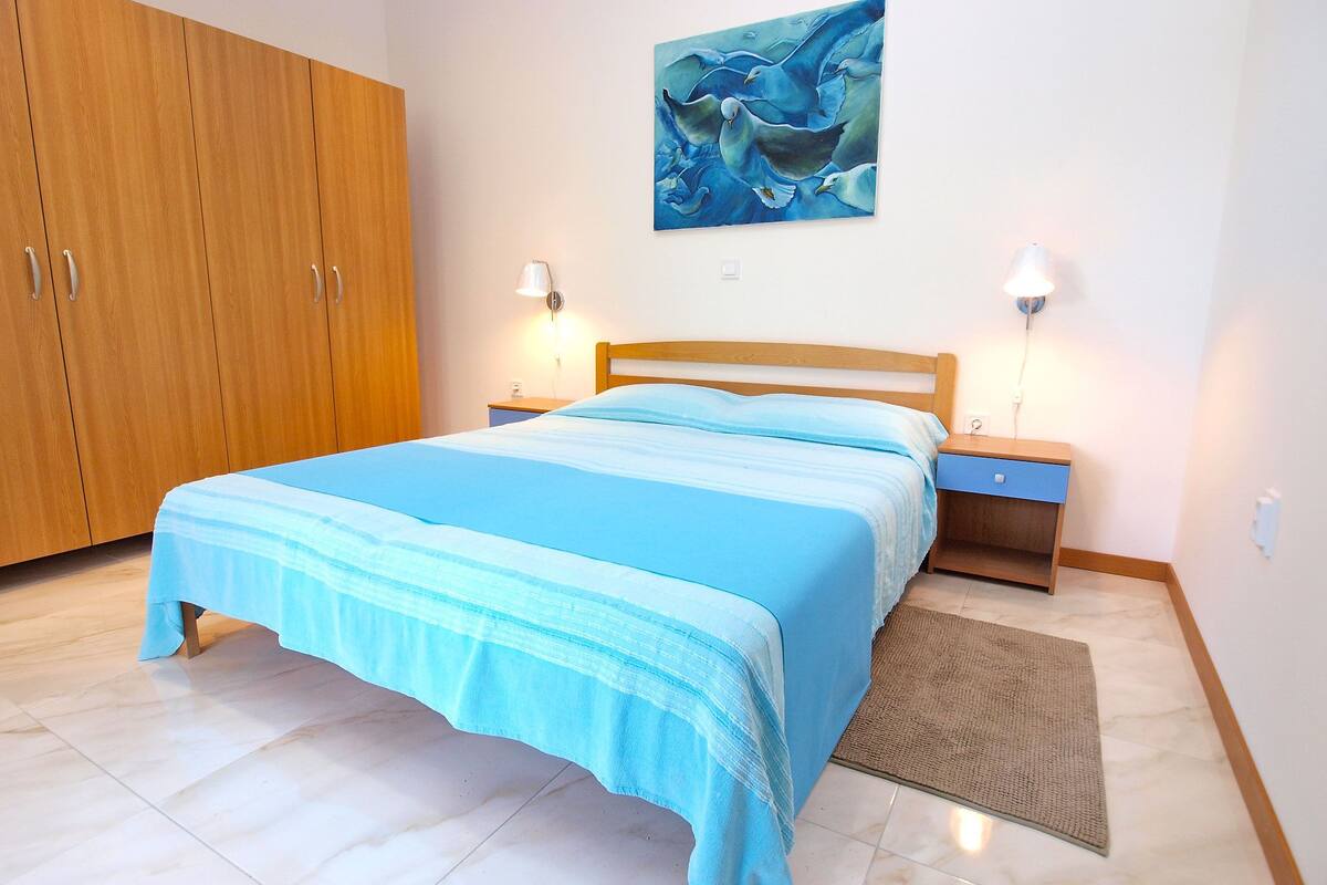 A bedroom with a bed, wooden wardrobe, bedside tables, and a painting on the wall.