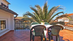 Eine Terrasse mit Tisch und Stühlen, einem Blumentopf und Blick auf ein Haus mit Ziegeldach.