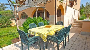 Une terrasse extérieure avec une table dressée pour quatre personnes, entourée de chaises vertes et recouverte d’une nappe à carreaux jaunes.