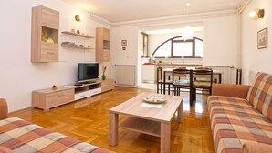 Una sala de estar moderna con televisión, muebles de madera, un comedor con mesa y sillas, y una cocina al fondo.