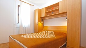 Une chambre à coucher de taille réduite, comprenant un lit, une armoire en bois et une petite étagère.