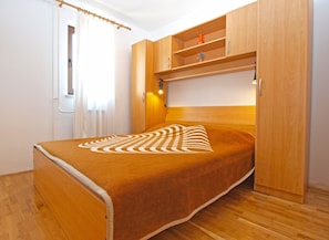 A compact bedroom with a bed, wooden wardrobe, and a small shelf. - Apartment 1316 (Pula)
