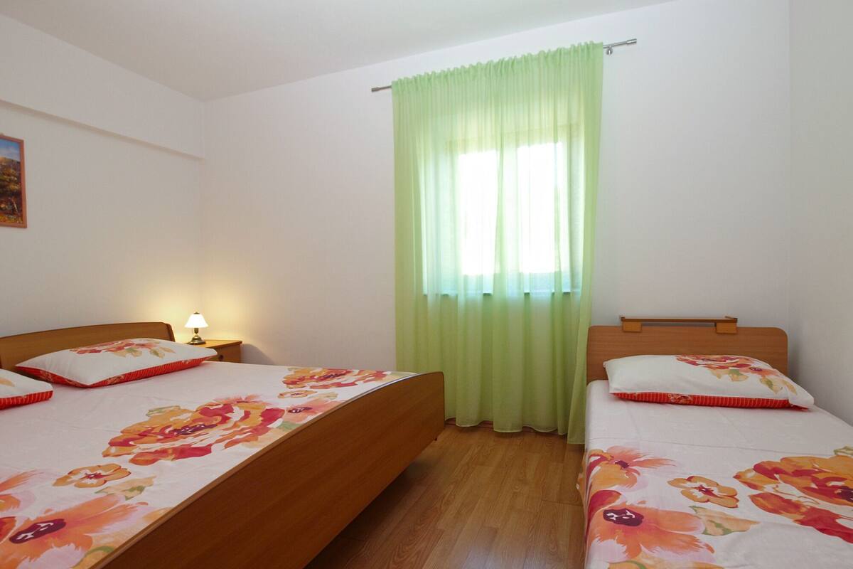 A bedroom with two beds, a nightstand, a lamp, and a window with green curtains.