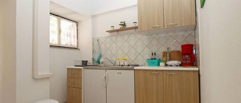 A compact kitchen with wooden cabinets, a small window, and basic appliances.