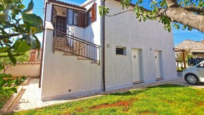 Un edificio de dos pisos con fachada blanca, una escalera visible y un ventanal pequeño.