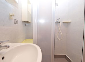 Un baño con un lavamanos blanco, una ducha con rociador manual y una alfombra de baño amarilla.