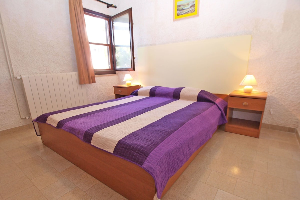 Un dormitorio con una cama, dos mesitas de noche, una ventana y un radiador.