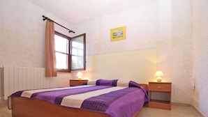 Un dormitorio con cama, dos mesitas de noche con lámparas, una ventana con cortinas y un cuadro colgado en la pared.