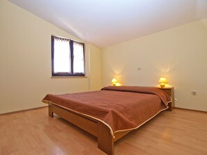 Un dormitorio con una cama de madera, dos lámparas de noche, un ventanal con cortinas y un interruptor de luz en la pared.
