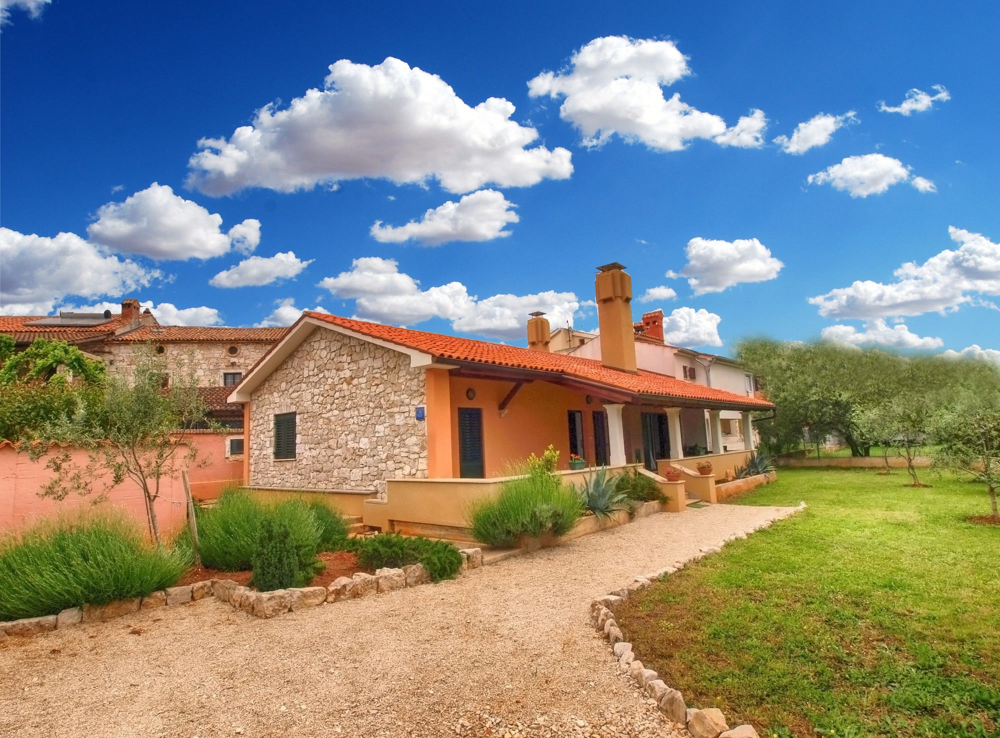 Uma casa de pedra com telhado de telhas vermelhas, um caminho de entrada de cascalho e um jardim bem cuidado.