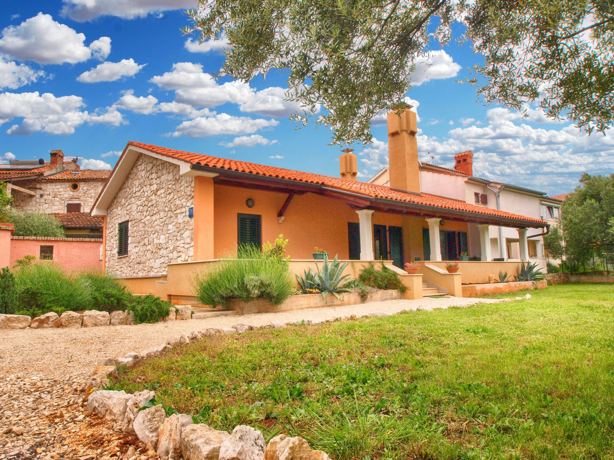 Ein traditionelles Haus im mediterranen Stil mit einer Steinaußenwand, einem Ziegeldach und einem gepflegten Garten mit einem Kiesweg zum Eingang.