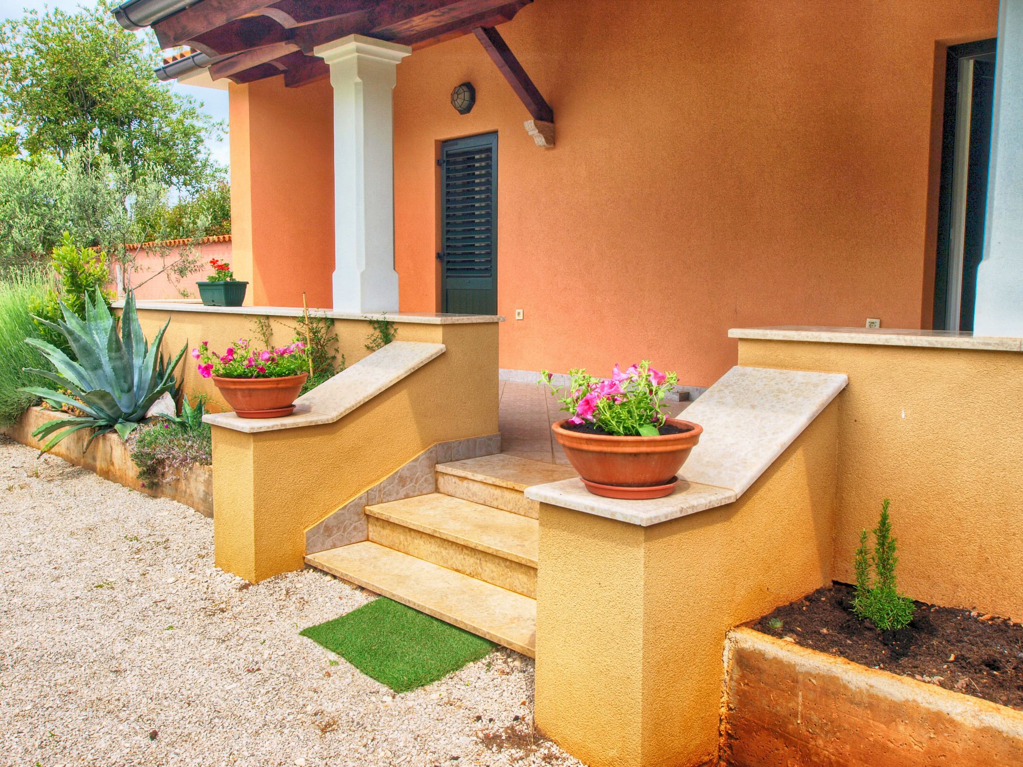 A building with a beige exterior, a set of outdoor stairs, and two potted plants with pink flowers.