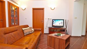 Ein Wohnzimmer mit braunem Ledersofa, einem Holztisch, einem Fernseher auf einem Holzschrank und einer Vitrine mit Glastüren.