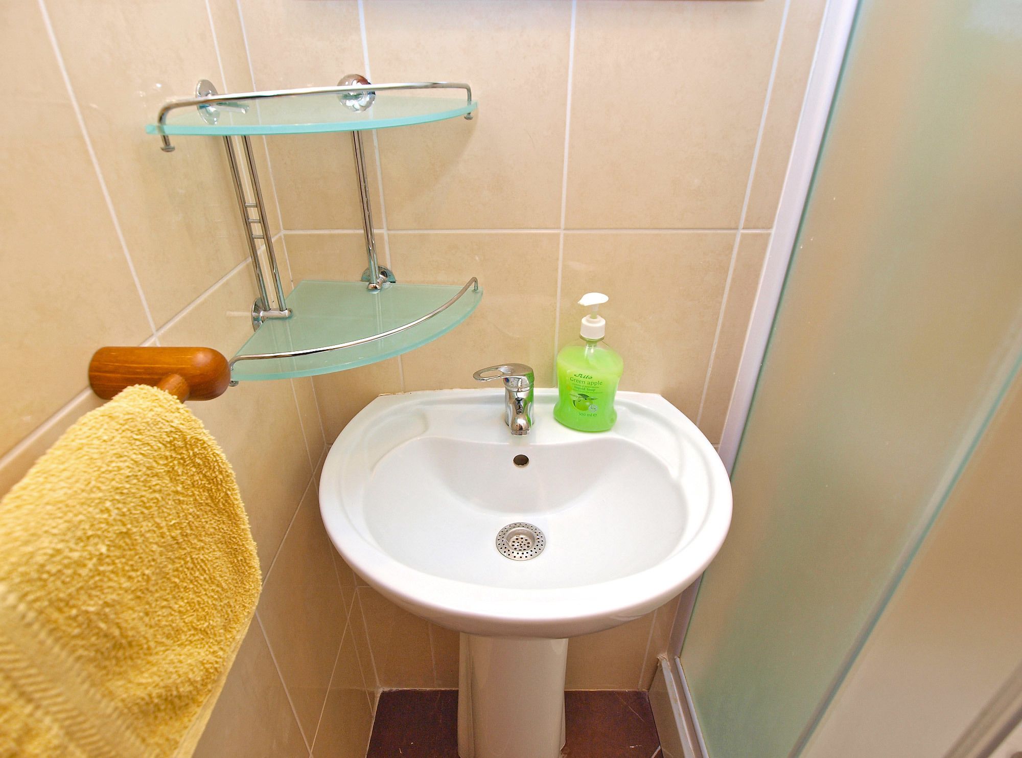 Een badkamer met een witte wasbak, een glazen plank, een gele handdoek en een groene zeepdispenser.