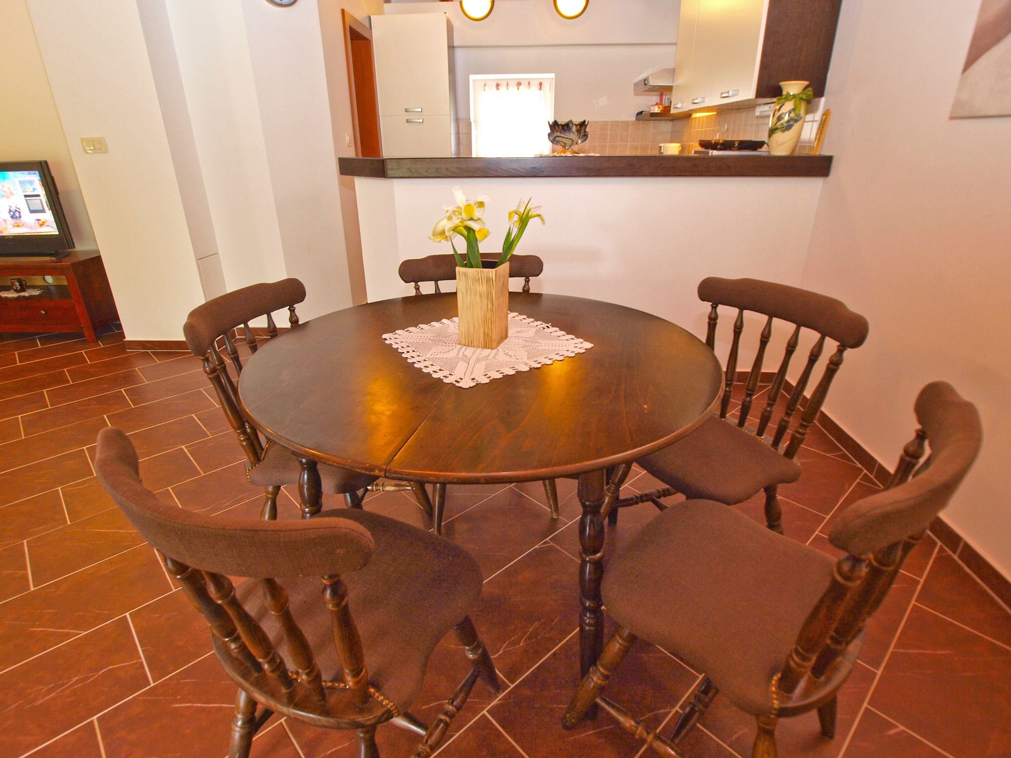 A dining area with a round wooden table, six chairs, and a vase with flowers.