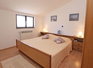 A bedroom with a wooden bed, two bedside tables with lamps, a window with blinds, and a radiator. - Apartment 1334 (Medulin)