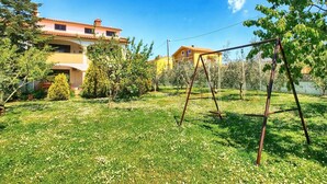 A residential area with a grassy lawn, a swing set, and buildings with red-tiled roofs. - Apartment 1334 (Medulin)
