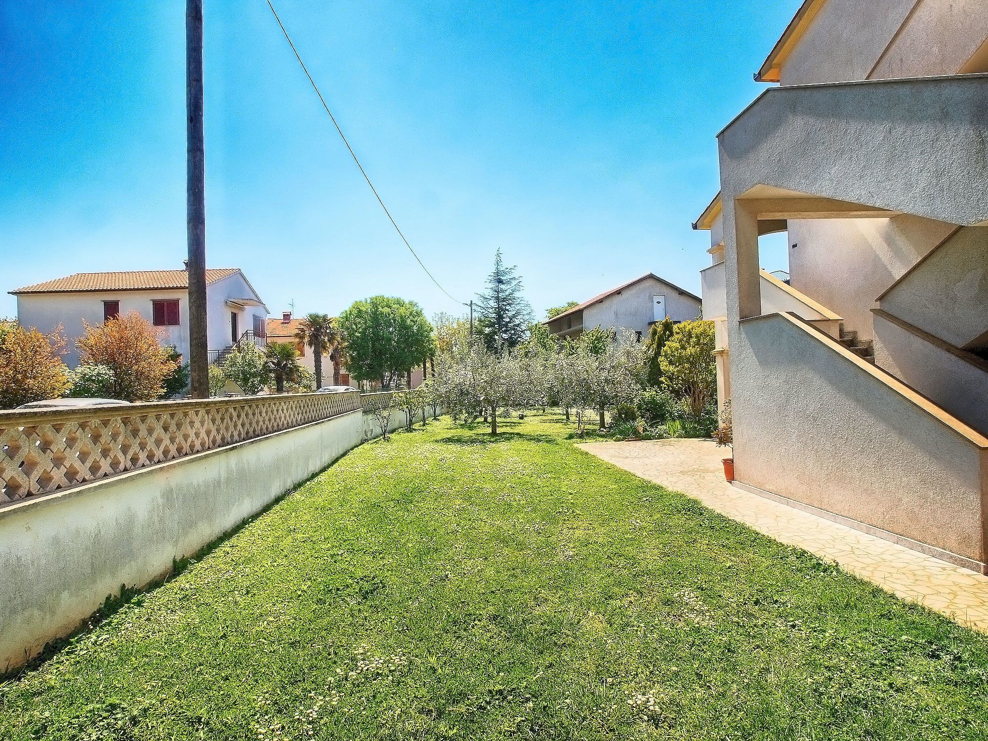 A residential area with a well-maintained lawn, a concrete wall, and houses with tiled roofs.