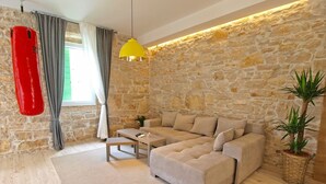 A living room with a stone wall, a sofa, a coffee table, a hanging punching bag, and a potted plant. - House 1338 (Pula)