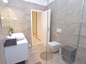 A modern bathroom with a white sink, toilet, and shower area. - House 1338 (Pula)