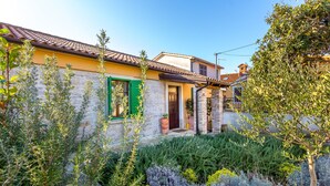 A traditional Mediterranean-style house with a stone facade, a tiled roof, and a well-maintained garden with various shrubs and a potted plant. - House 1338 (Pula)