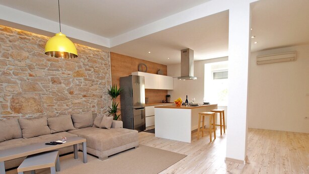 A modern living room with a stone wall, a sofa, a coffee table, and a yellow pendant light. - House 1338 (Pula)