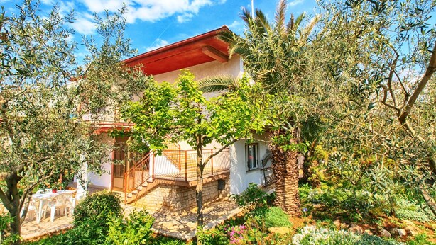 A house with a red roof, surrounded by lush greenery and a stone pathway leading to the entrance. - Apartment 1341 (Pula)