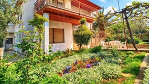A two-story house with a balcony, surrounded by a garden with various plants and flowers. - Apartment 1341 (Pula)