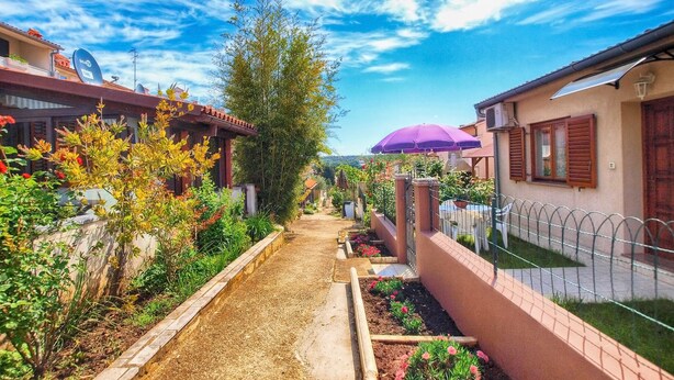 Un estrecho sendero bordeado por edificios con jardines y una sombrilla morada.
