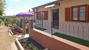 Un edificio residencial con jardín cercado, un paraguas morado y cielo despejado.