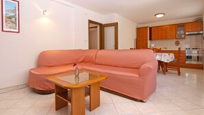 Una sala de estar con un sofá rosa, una mesa de centro de vidrio y una cocina al fondo.