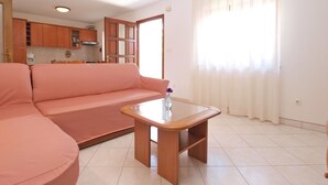 Una sala de estar con un sofá rosa, una mesa de centro de madera y una cocina al fondo.