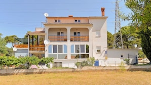 A two-story building with a balcony on the upper floor, a satellite dish on the roof, and a power line tower in the background. - Apartment 1355 (Pula)