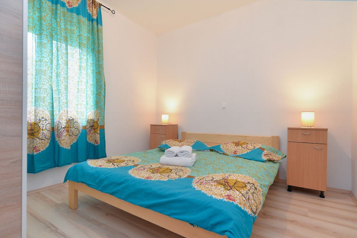A bedroom with a bed, two bedside tables, a nightstand, and a window with curtains.