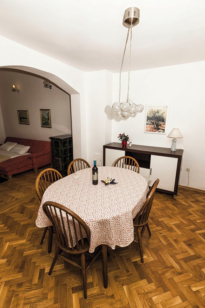 Un comedor con una mesa redonda, sillas, una lámpara colgante, un mueble bajo y un sofá al fondo.