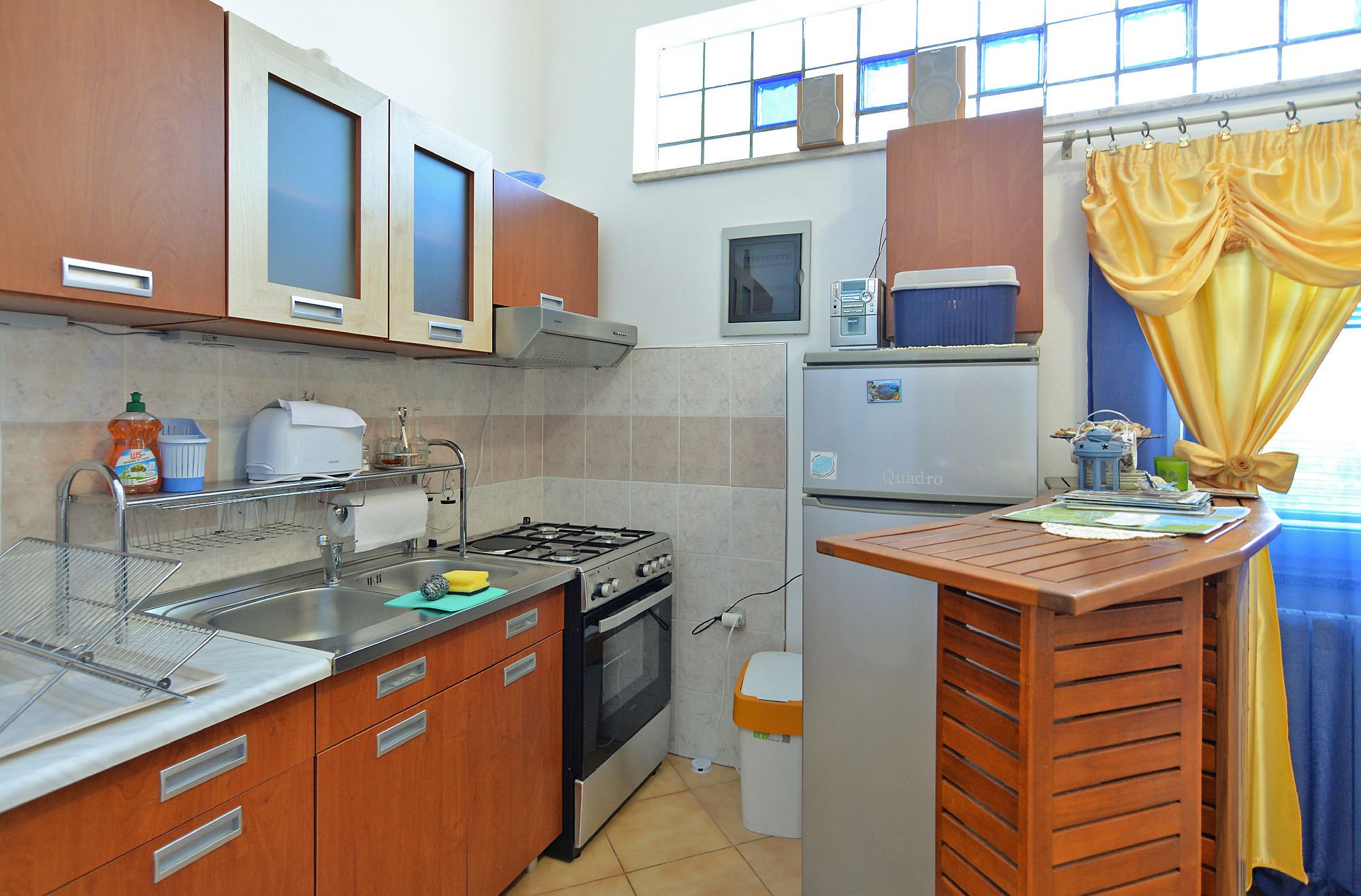 A compact kitchen with wooden cabinets, a gas stove, a microwave, and a small refrigerator.