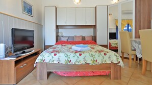 Quarto com cama, televisão, escrivaninha e cadeira.