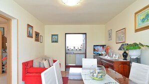 A living room with a red sofa, white chairs, a dining table with a vase, and a kitchen in the background. - Apartment 1375 (Fazana)