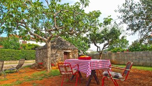 A rustic outdoor dining area with a stone wall, a small tree, and a checkered tablecloth. - House 1378 (Vodnjan)