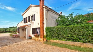 A two-story house with a brick chimney, a small porch with a table and chairs, and a well-maintained hedge. - House 1378 (Vodnjan)