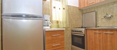 Cocina compacta con refrigerador, microondas, cafetera, estufa, horno y armarios de madera.