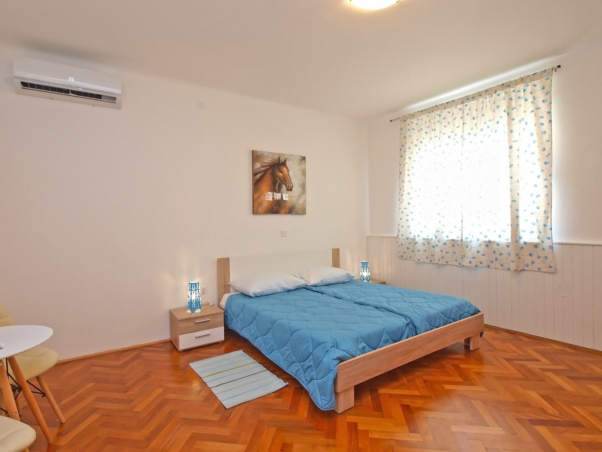 A bedroom with a wooden bed, a nightstand, a small table, and a window with curtains.
