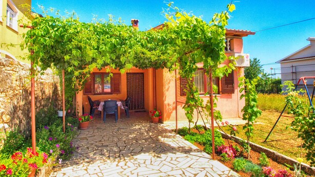A courtyard with a stone pathway, a table and chairs under a vine-covered pergola, and a garden with various plants and flowers. - Apartment 1382 (Marcana)