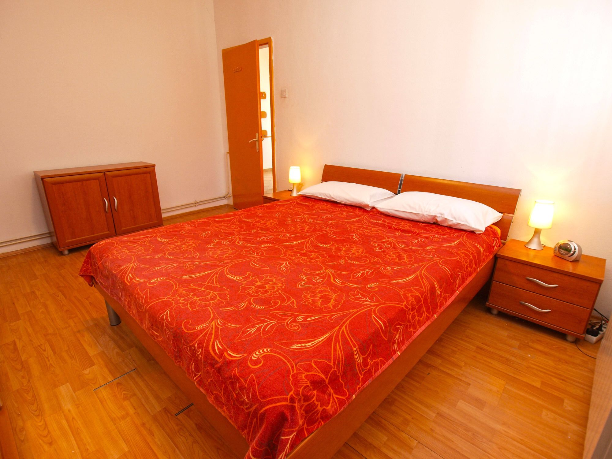 A neatly made bed with a red floral bedspread, a wooden headboard, and two bedside tables with lamps.