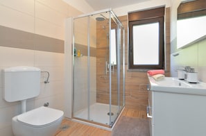 Et moderne badeværelse med en glasafskærmet brusekabine, toilet og et håndvaskarrangement med spejl.