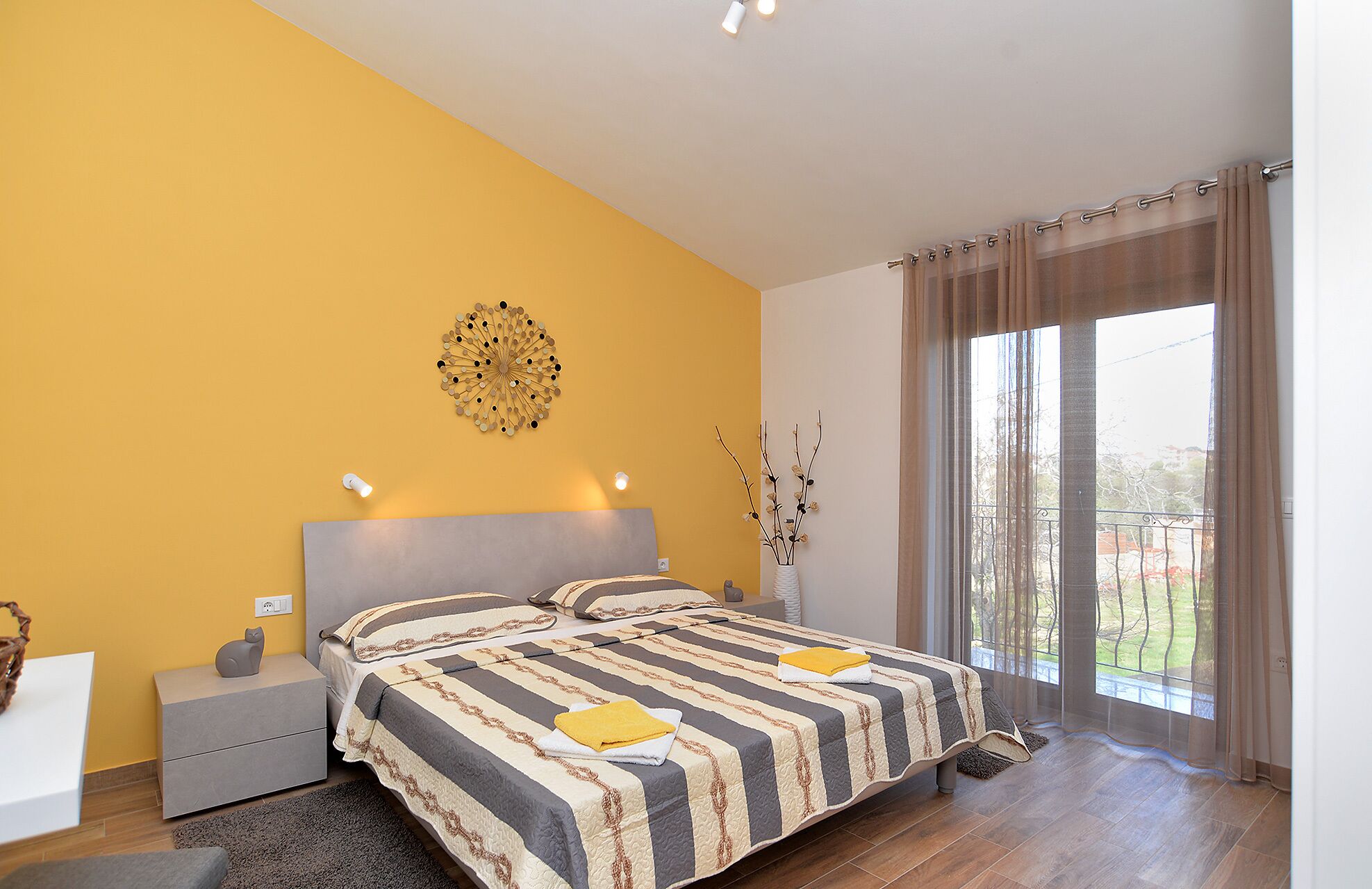 A bedroom with a bed, bedside tables, a decorative wall piece, and a view of the outdoors.